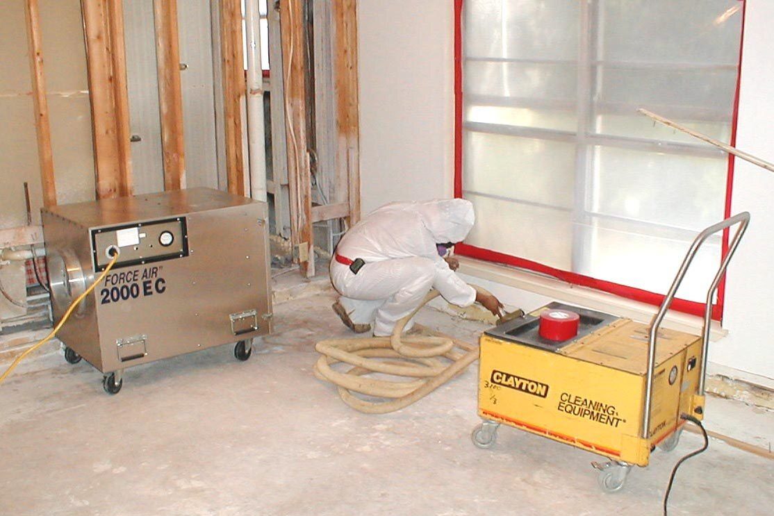 Technician inside a sealed containment with a negative-air machine and HEPA vacuum