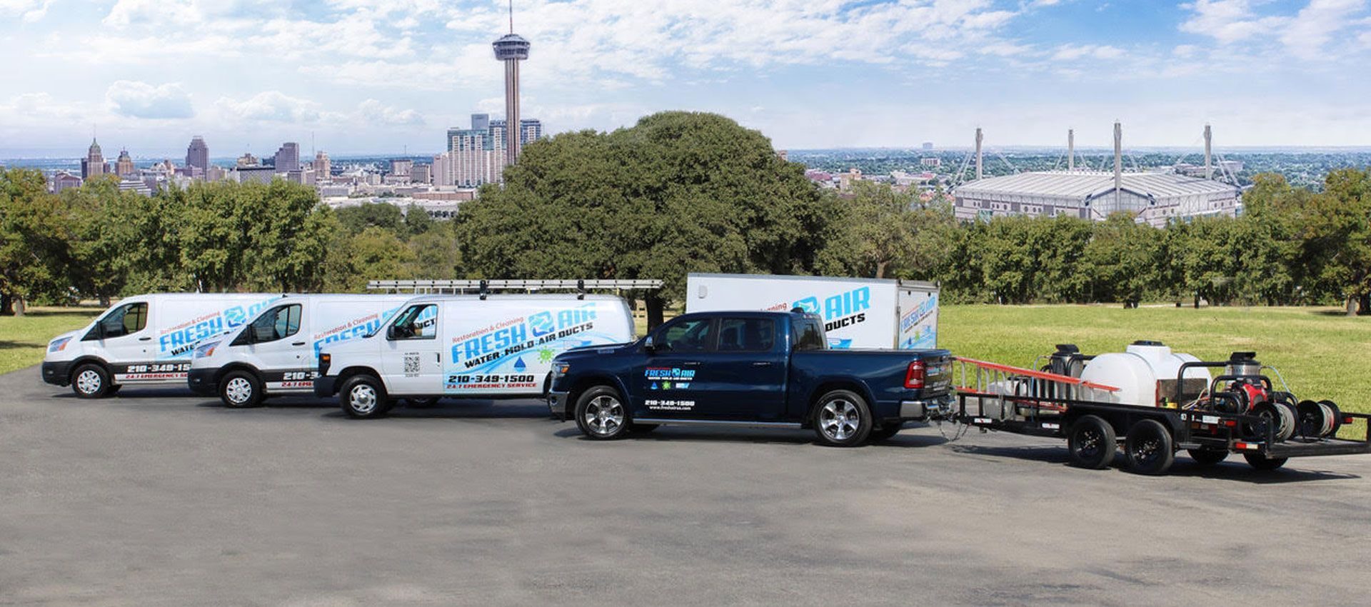 Fresh Air Restoration & Cleaning vans, box truck and pressure-washing trailer lined up in front of the San Antonio skyline and the Tower of the Americas