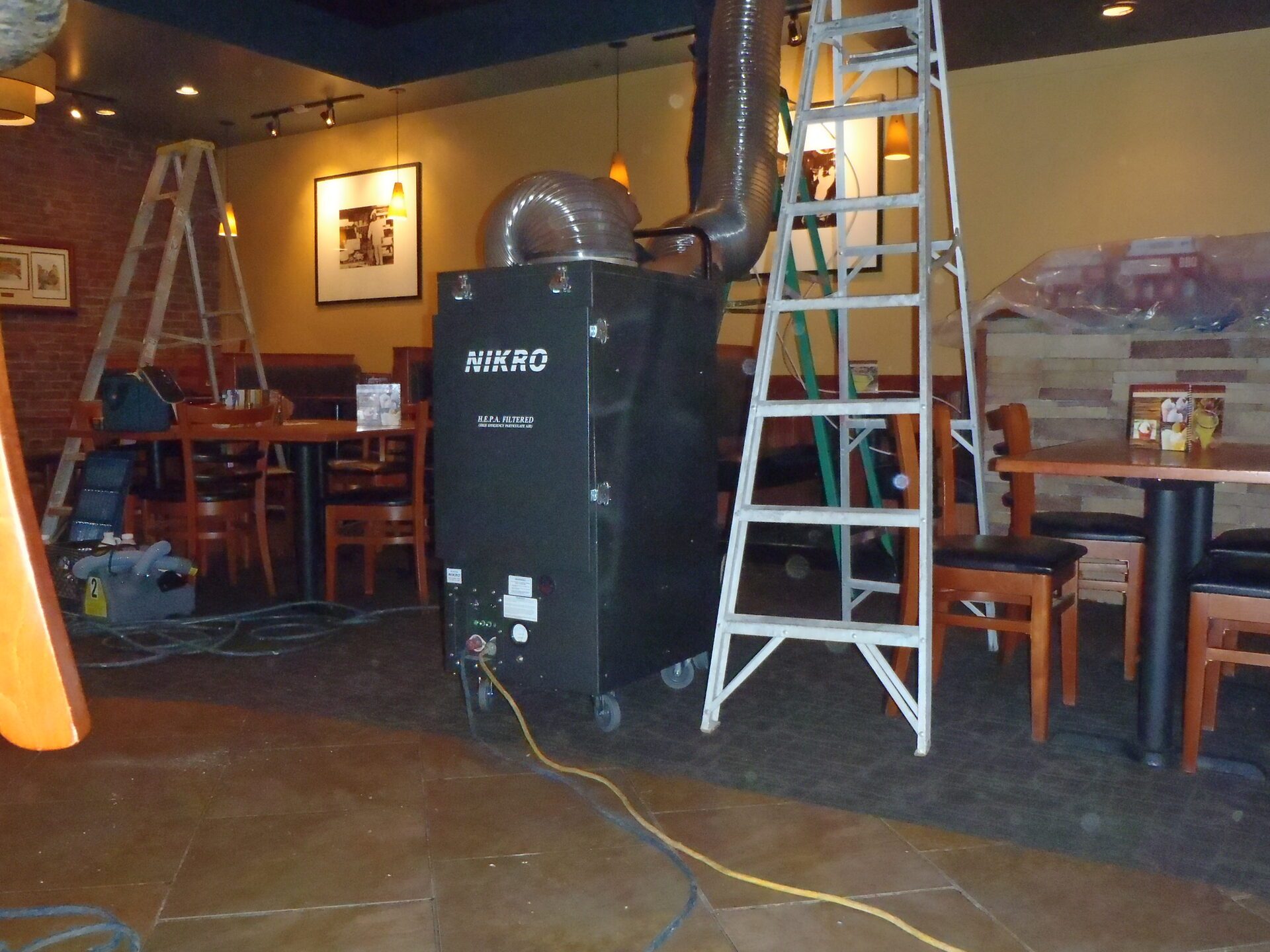HEPA-filtered air scrubber and ladders set up for duct cleaning inside a restaurant dining room